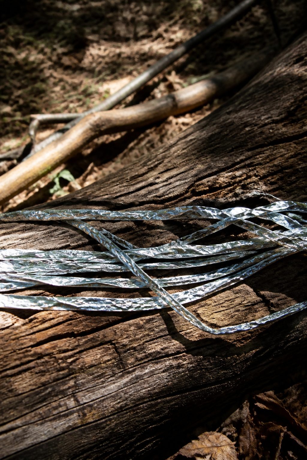 Mylar Blanket Uses: 38 Practical Ideas for Emergencies & Daily Life (2026) 29 Rough mylar strips laid out on a log, resembling makeshift rope.